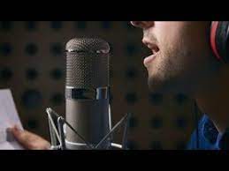 Homem sorrindo cantando em um estúdio de gravação com microfone e fones de ouvido, com iluminação profissional.