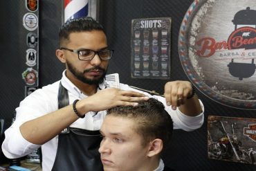 Homem recebendo corte de cabelo em barbearia moderna, close-up em ferramentas de barbeiro.